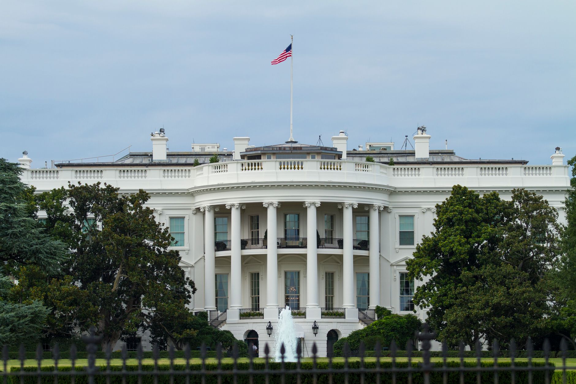 Front view of the iconic White House with the American flag, surrounded by greenery.