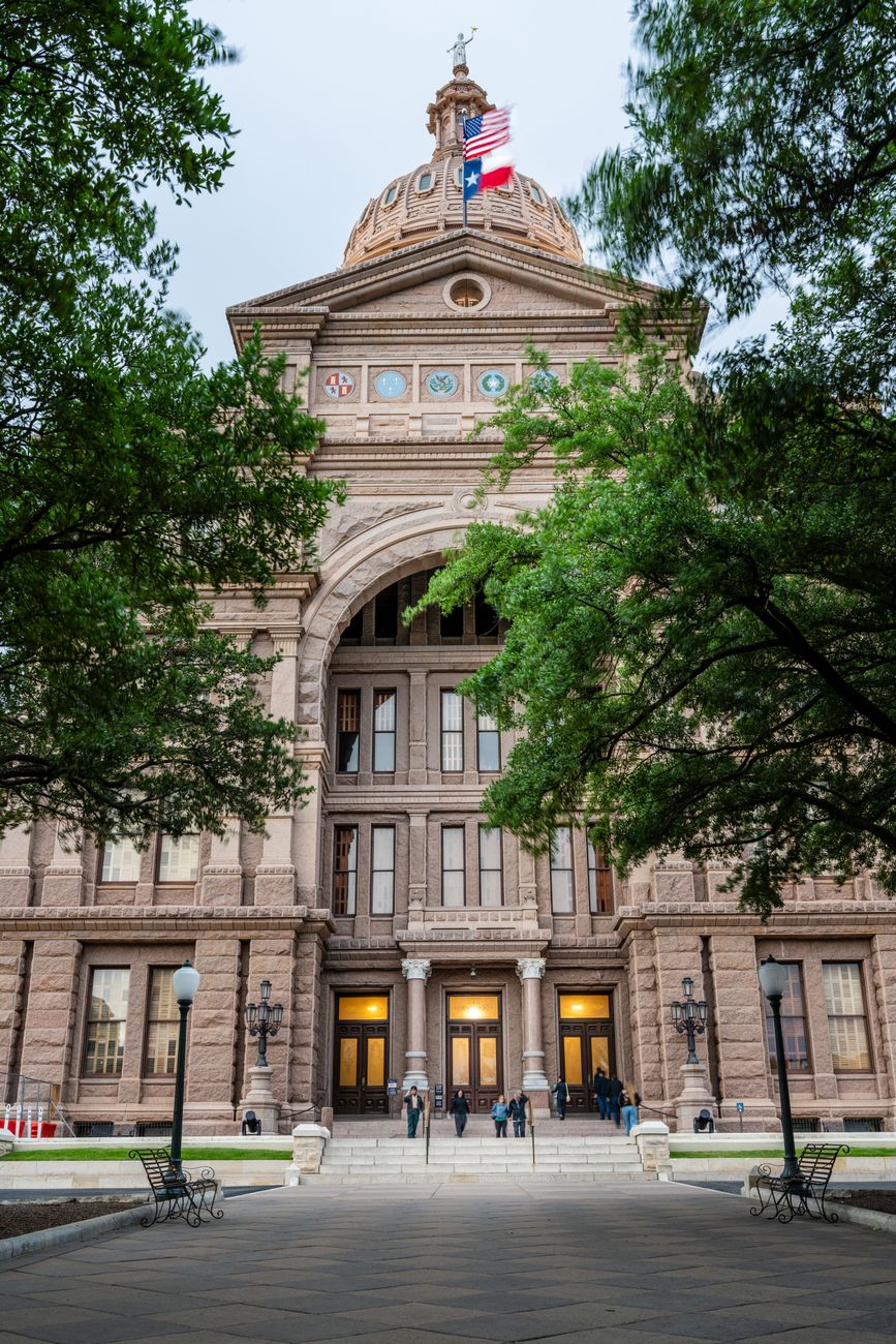 Front view of the iconic Texas State Capitol building in Austin surrounded by trees.